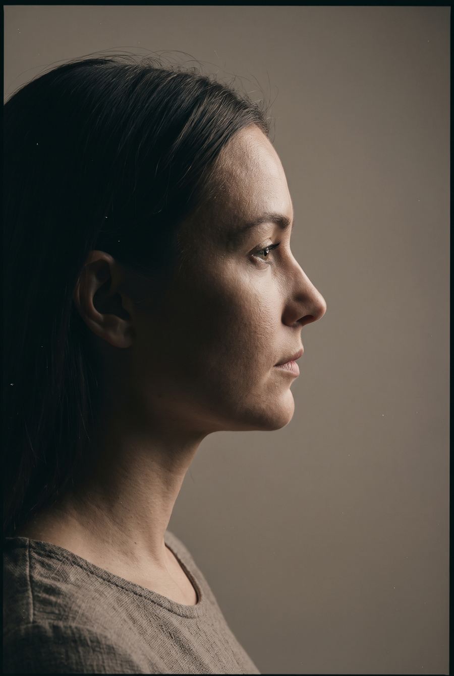 A studio portrait of a woman in profile against a warm grey backdrop.