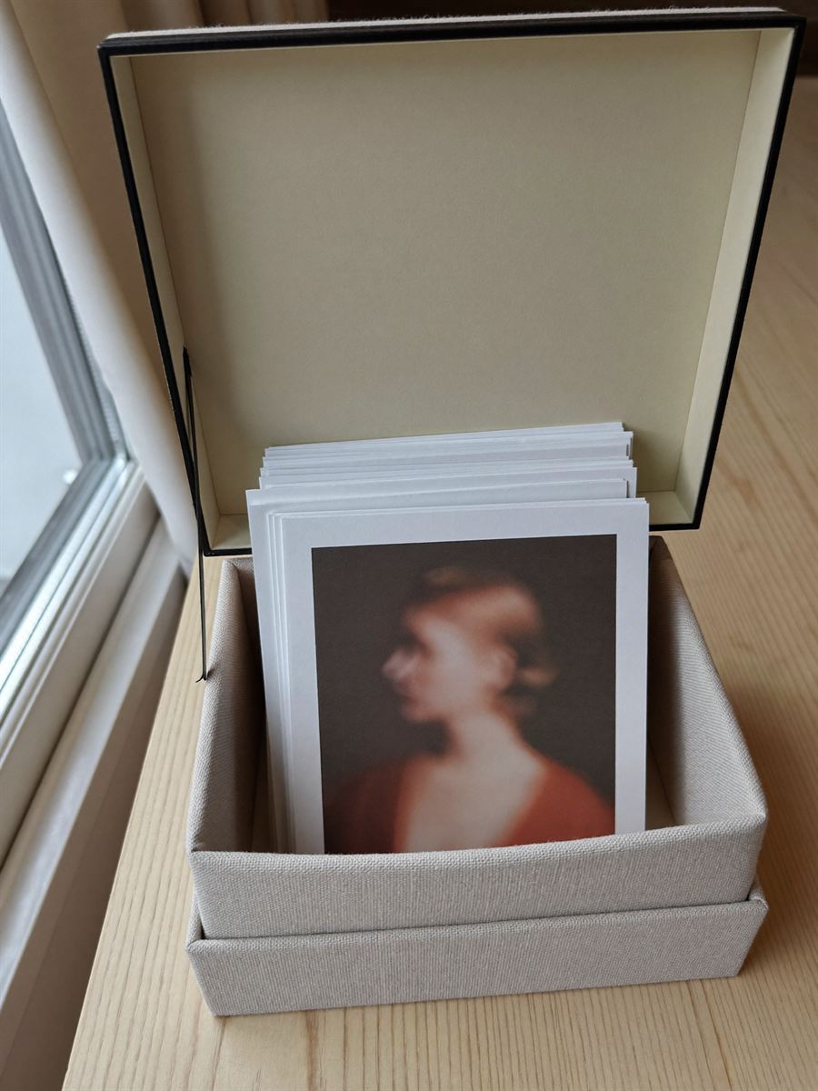 A stack of printed matte photographs in an open linen-covered presentation box on a pale table.