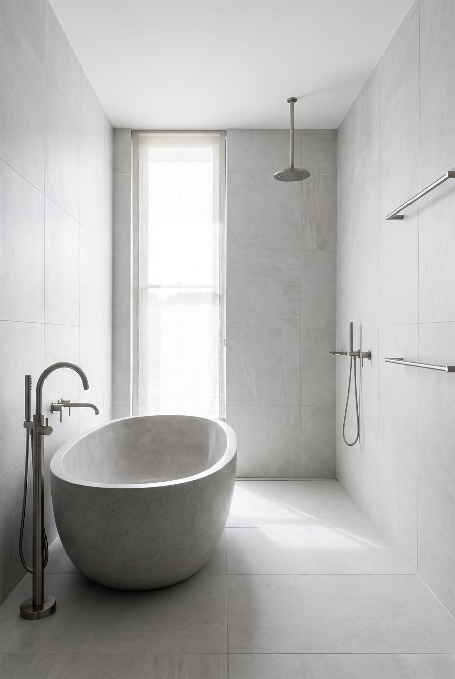 A modern bathroom with a freestanding stone bath and a tall narrow window.