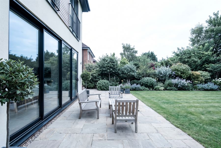 A paved rear terrace with outdoor seating opening onto a lawn and mature planting.