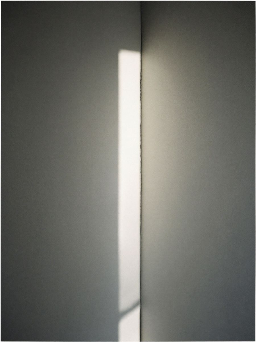 Raking afternoon sunlight falling across a plain white wall meeting a pale oak edge.